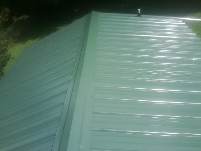 New green metal panels meeting at the ridge of a roof — Flat Roof Repair work by our crew in Goodlettsville