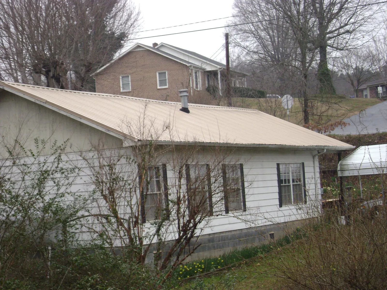 Tan metal roof on a white sided house set into a hillside — Commercial Roofing by Roofing Brothers in Goodlettsville